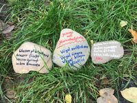 Foto von drei faustgroßen Steinen im Gras, die mit Gedichten beschrieben sind